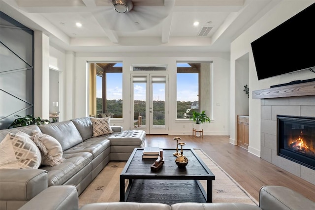 living room with light wood finished floors, visible vents, coffered ceiling, a tile fireplace, and french doors