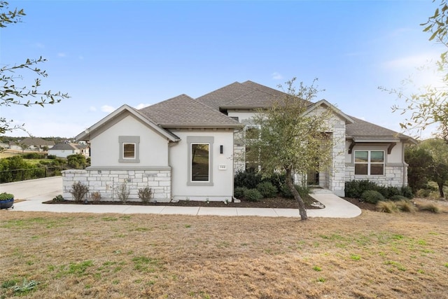 view of front of house with a front yard, stone siding, roof with shingles, and stucco siding