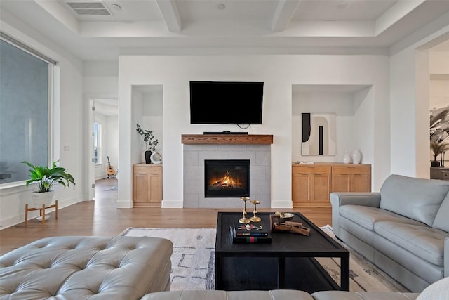 living room featuring light wood-style floors, a tile fireplace, visible vents, and beamed ceiling