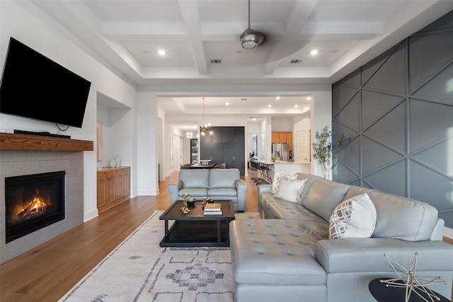 living room with a fireplace, visible vents, light wood-style floors, coffered ceiling, and beamed ceiling