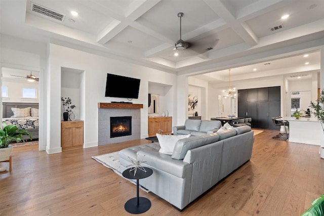 living room with ceiling fan with notable chandelier, coffered ceiling, visible vents, and light wood-style floors