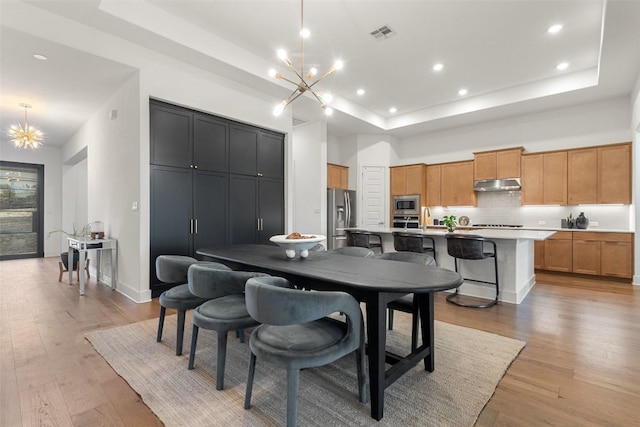 dining area featuring a tray ceiling, light wood-style floors, visible vents, and a notable chandelier