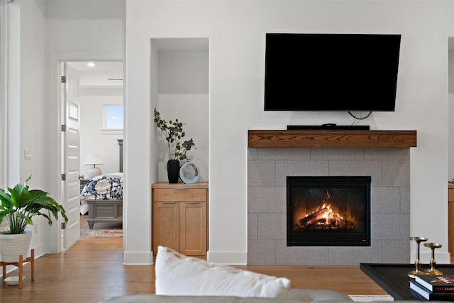 living area with baseboards, a tiled fireplace, and wood finished floors