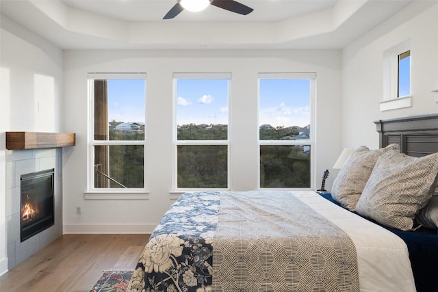 bedroom featuring a tray ceiling, multiple windows, a fireplace, and wood finished floors