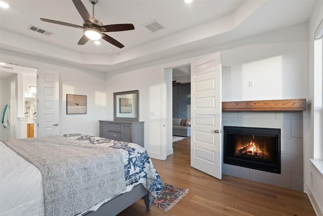 bedroom featuring a tray ceiling, a fireplace, wood finished floors, and visible vents