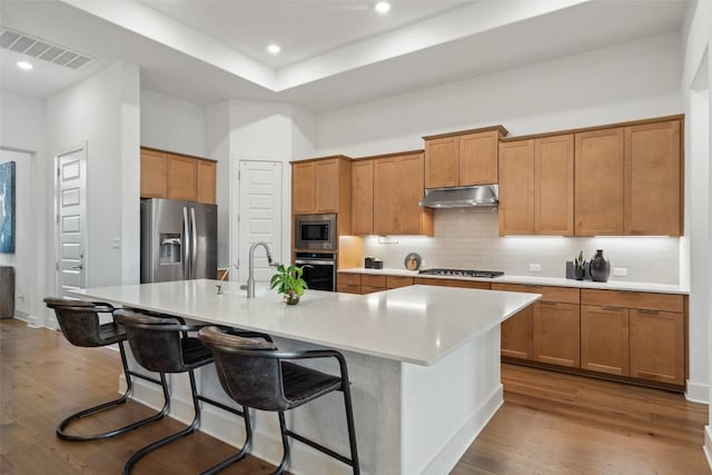 kitchen with under cabinet range hood, visible vents, a center island with sink, stainless steel appliances, and wood finished floors