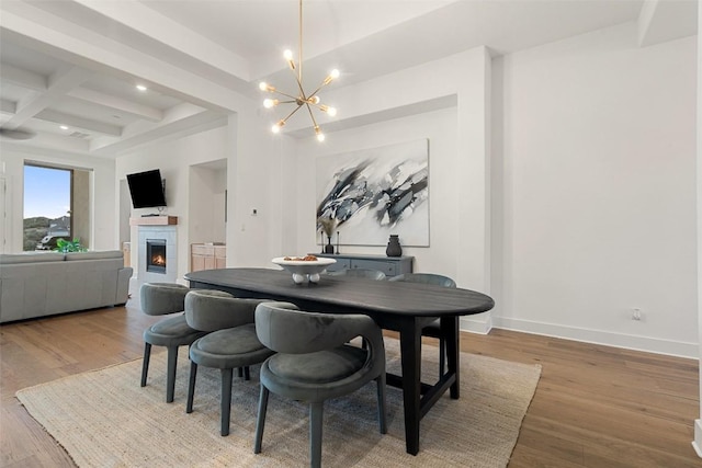 dining area featuring beam ceiling, wood finished floors, coffered ceiling, a lit fireplace, and baseboards