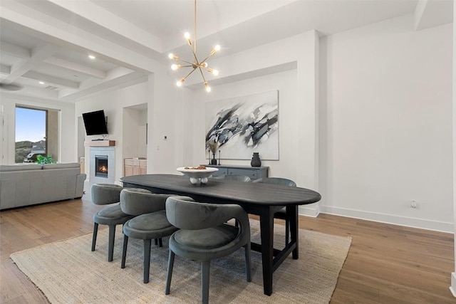 dining space with wood finished floors, a warm lit fireplace, beamed ceiling, coffered ceiling, and a notable chandelier