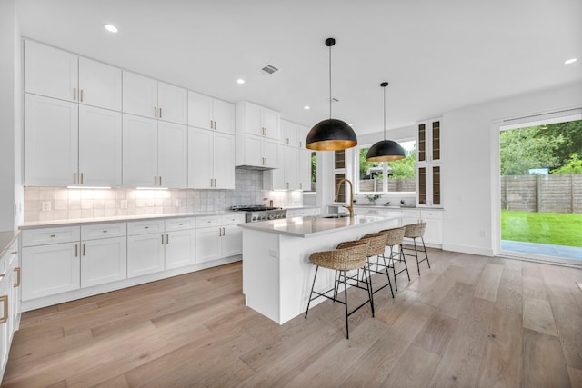 kitchen with light wood finished floors, white cabinetry, visible vents, and decorative backsplash