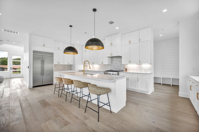 kitchen with visible vents, backsplash, a sink, stainless steel built in refrigerator, and range