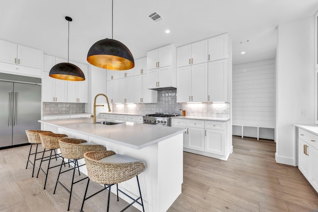 kitchen with appliances with stainless steel finishes, light wood-type flooring, a sink, and tasteful backsplash