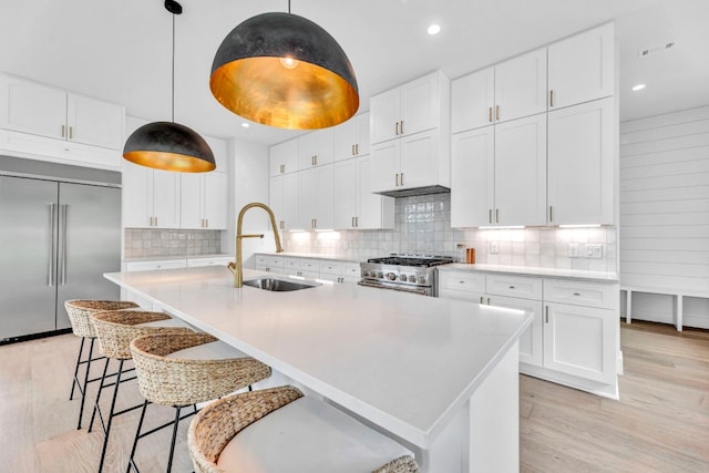 kitchen featuring a sink, high quality appliances, light wood-type flooring, tasteful backsplash, and an island with sink