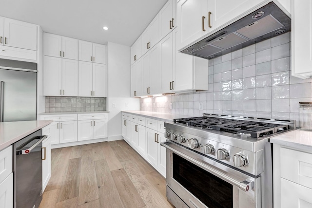 kitchen with light wood finished floors, decorative backsplash, high quality appliances, light countertops, and under cabinet range hood