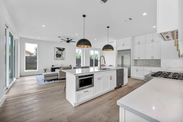 kitchen featuring light wood-type flooring, tasteful backsplash, appliances with stainless steel finishes, and a sink