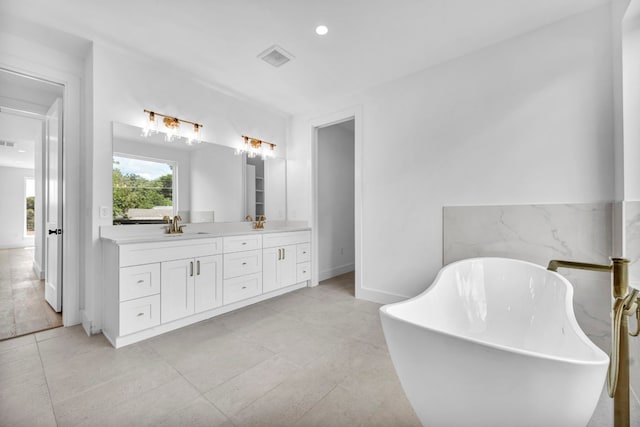 bathroom with visible vents, a sink, a freestanding bath, and double vanity