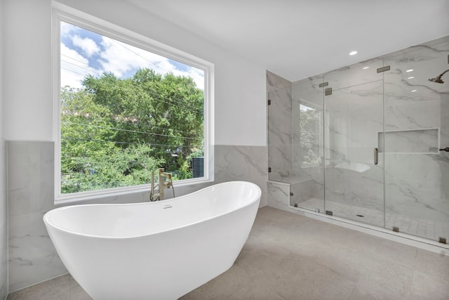 full bath with a soaking tub, plenty of natural light, a marble finish shower, and tile walls