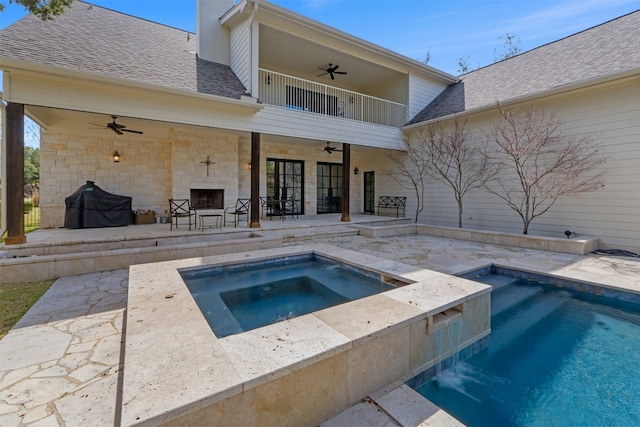 rear view of property with a patio, exterior fireplace, a balcony, a shingled roof, and a ceiling fan