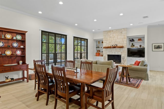 dining space with french doors, crown molding, light wood-style floors, a stone fireplace, and baseboards