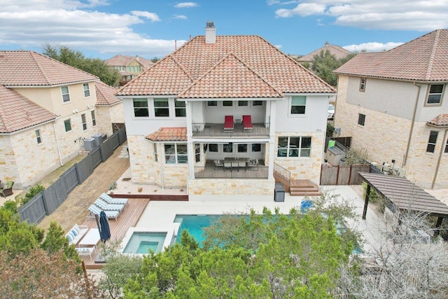 rear view of property with a balcony, a tile roof, a chimney, a fenced backyard, and a patio area