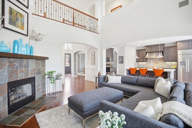 living area featuring arched walkways, a fireplace, visible vents, baseboards, and dark wood-style floors