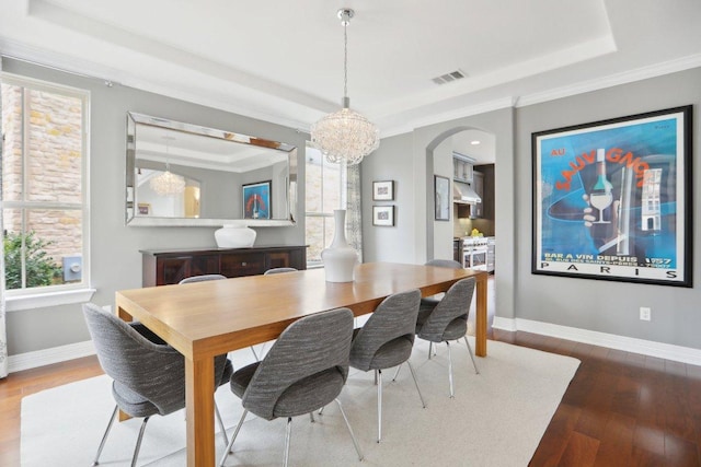 dining room featuring baseboards, visible vents, a raised ceiling, arched walkways, and wood finished floors