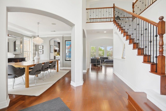 entryway with a towering ceiling, wood finished floors, a chandelier, baseboards, and stairs