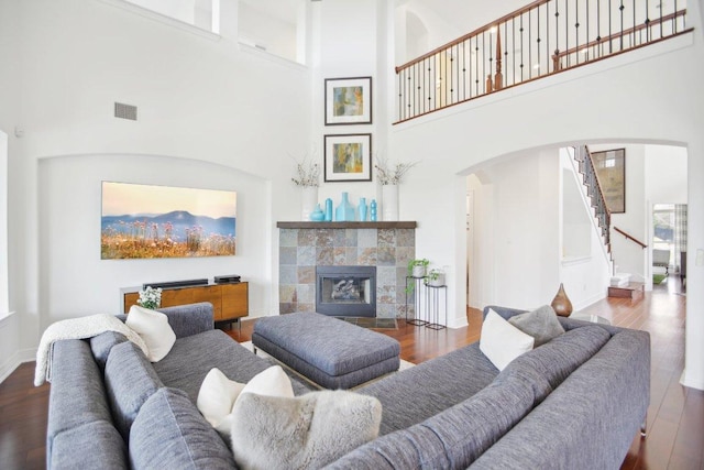 living room featuring arched walkways, visible vents, wood finished floors, a tile fireplace, and baseboards