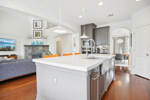 kitchen with arched walkways, visible vents, light countertops, dark wood-style floors, and dishwasher