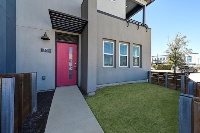 entrance to property with stucco siding, a yard, and fence