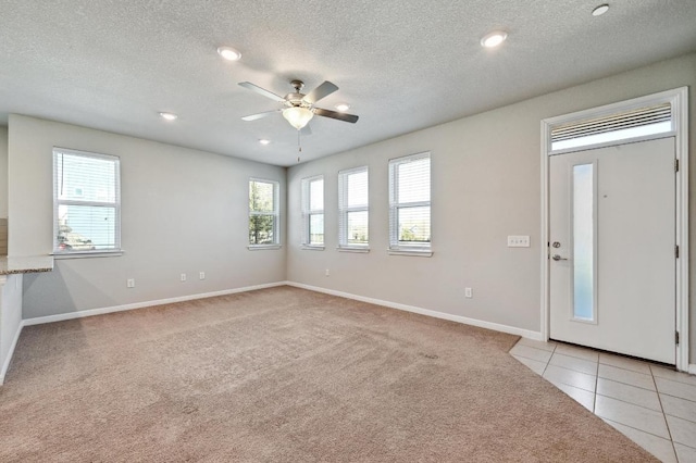 interior space with light colored carpet, a ceiling fan, light tile patterned flooring, a textured ceiling, and baseboards