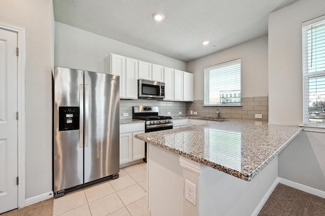 kitchen featuring a peninsula, appliances with stainless steel finishes, white cabinetry, and decorative backsplash