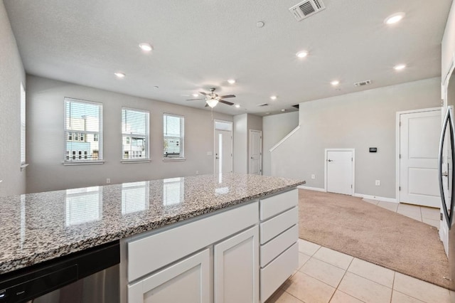 kitchen with light tile patterned floors, visible vents, stainless steel dishwasher, and light colored carpet