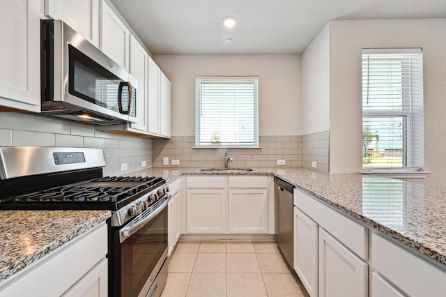 kitchen with light tile patterned floors, a sink, white cabinetry, appliances with stainless steel finishes, and decorative backsplash