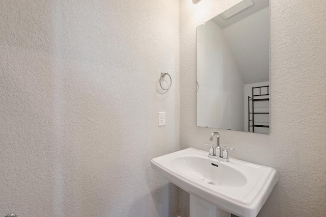 bathroom with lofted ceiling, a sink, and a textured wall