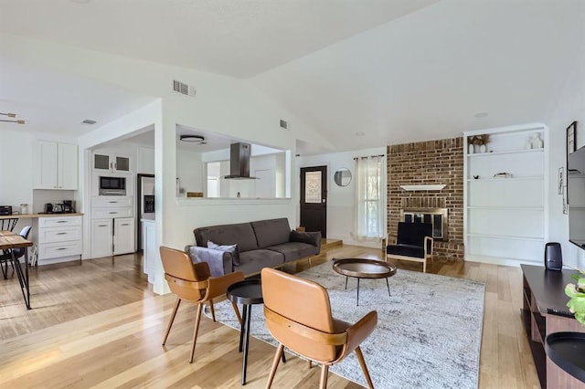 living area with lofted ceiling, light wood finished floors, a brick fireplace, and visible vents