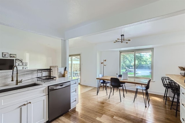 kitchen with light wood-style floors, white cabinetry, a sink, dishwasher, and baseboards