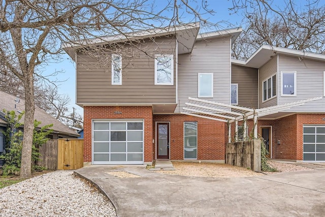 view of front of house featuring brick siding, driveway, an attached garage, and fence