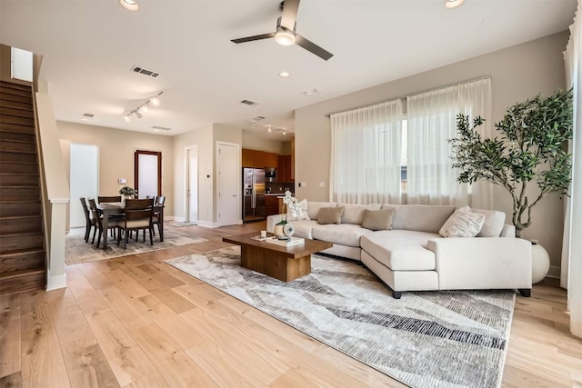 living room with a ceiling fan, visible vents, stairs, light wood-style floors, and track lighting