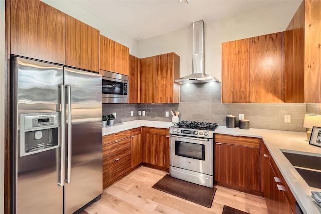 kitchen featuring appliances with stainless steel finishes, wall chimney range hood, light wood-style floors, and brown cabinets