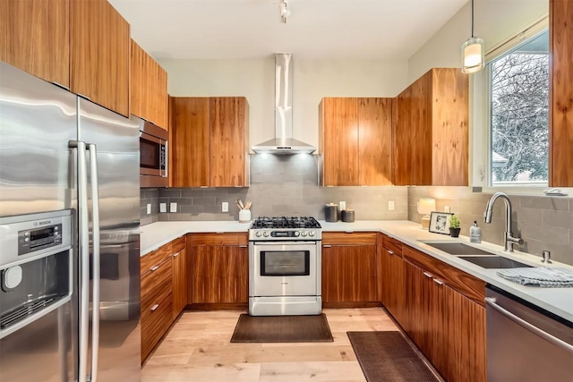 kitchen with stainless steel appliances, brown cabinets, a sink, and wall chimney exhaust hood