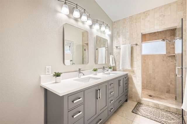 bathroom featuring double vanity, tile patterned flooring, a tile shower, and a sink