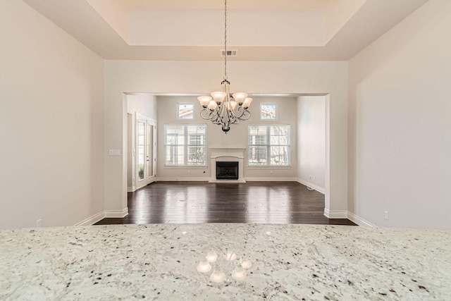 304 Belforte Ave, Austin, TX 78734 - unfurnished living room featuring a chandelier, dark wood-type flooring, a tray ceiling, a fireplace with raised hearth, and baseboards
