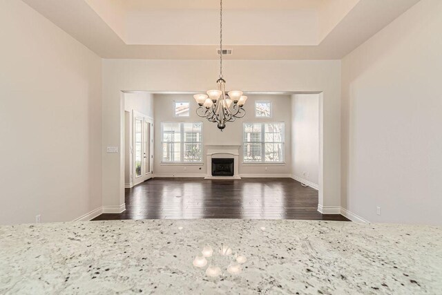 304 Belforte Ave, Austin, TX 78734 - unfurnished living room featuring a chandelier, dark wood-type flooring, a tray ceiling, a fireplace with raised hearth, and baseboards
