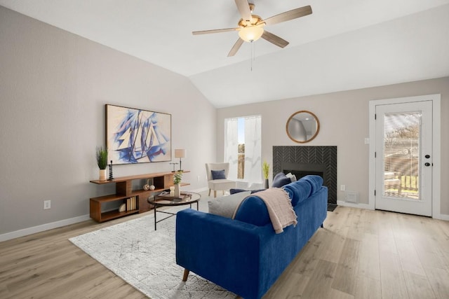 living room featuring lofted ceiling, light wood-style floors, a ceiling fan, a tile fireplace, and baseboards