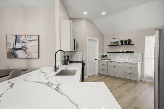 kitchen with lofted ceiling, light wood-style floors, light stone counters, and a sink