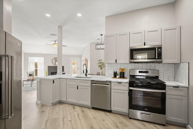 kitchen with a peninsula, a sink, a ceiling fan, appliances with stainless steel finishes, and backsplash