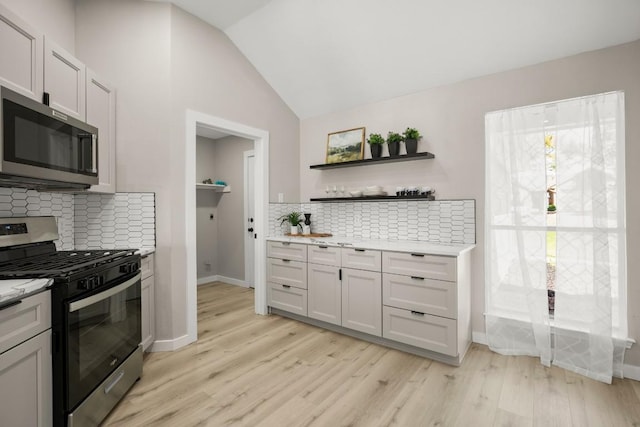 kitchen featuring lofted ceiling, stainless steel appliances, light countertops, open shelves, and light wood finished floors