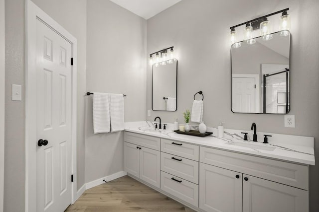 bathroom with double vanity, a sink, baseboards, and wood finished floors