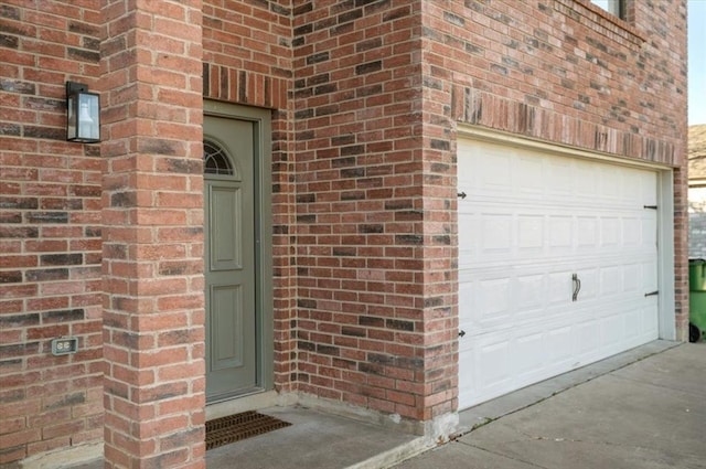 property entrance with a garage, driveway, and brick siding