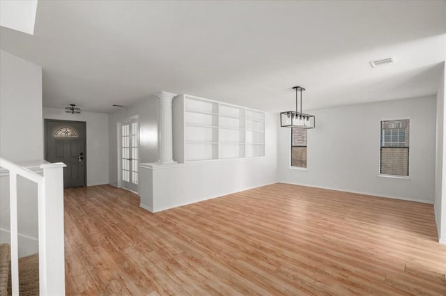 empty room featuring light wood-style floors, visible vents, stairway, and ornate columns